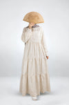 Person wearing a long beige dress holding a wooden fan on a white background