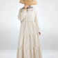 Person wearing a long beige dress holding a wooden fan on a white background